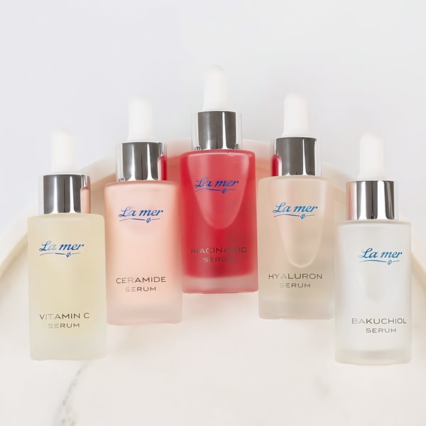 This creative showcases five distinct serums arranged symmetrically on a clean, professional studio-lit surface.